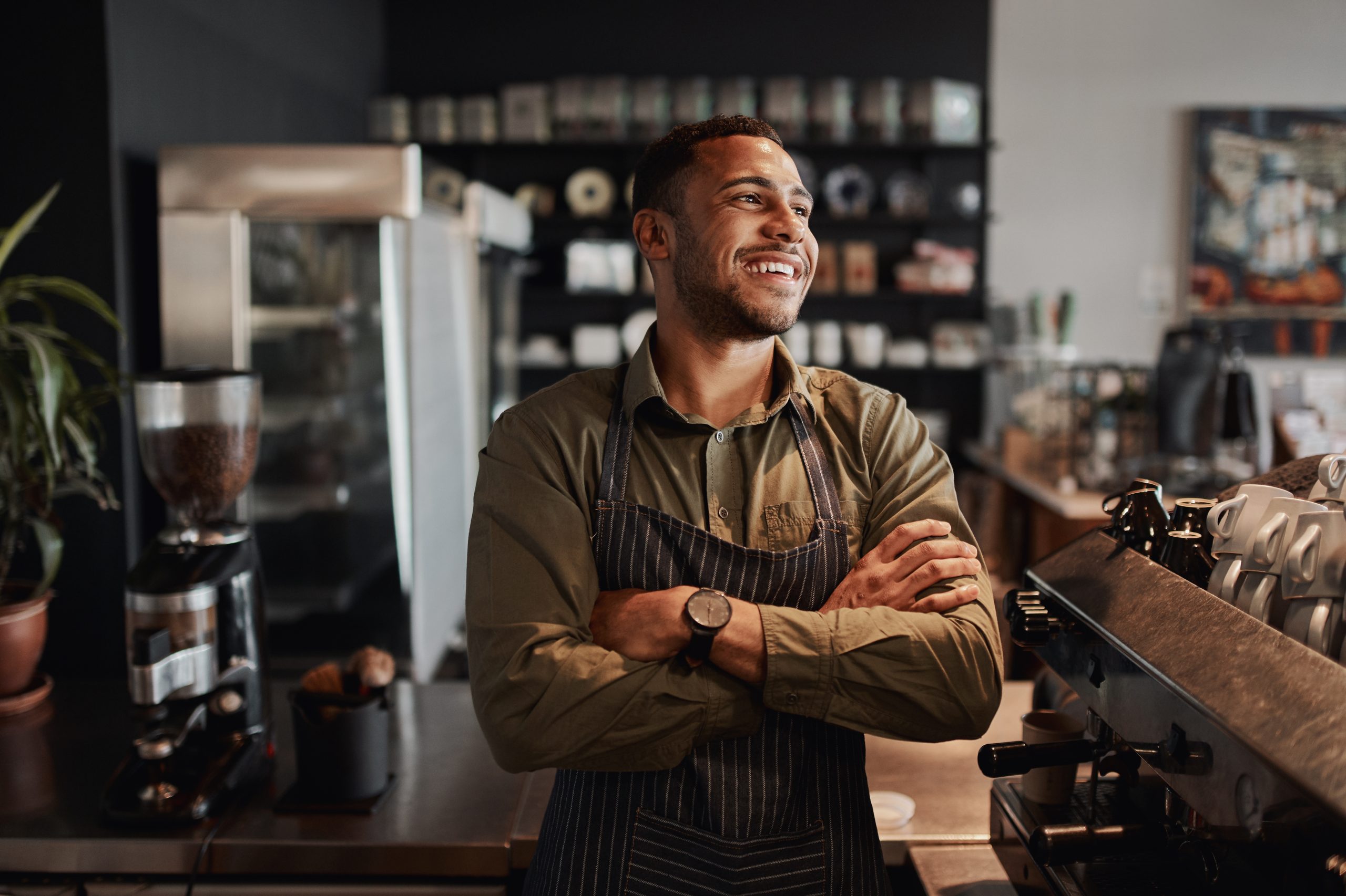 Successful handsome male cafe owner standing with arms crossed looking away thinking about future