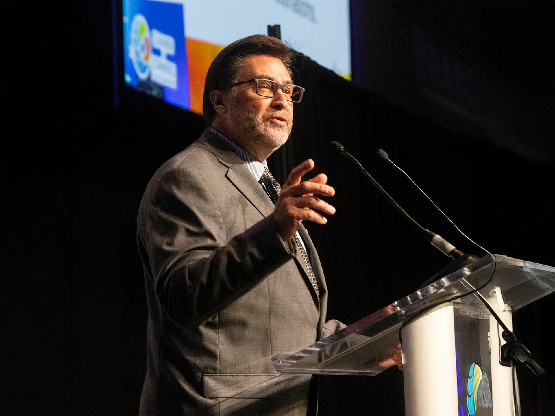 Speaker in a suit and tie delivers a speech at a podium.