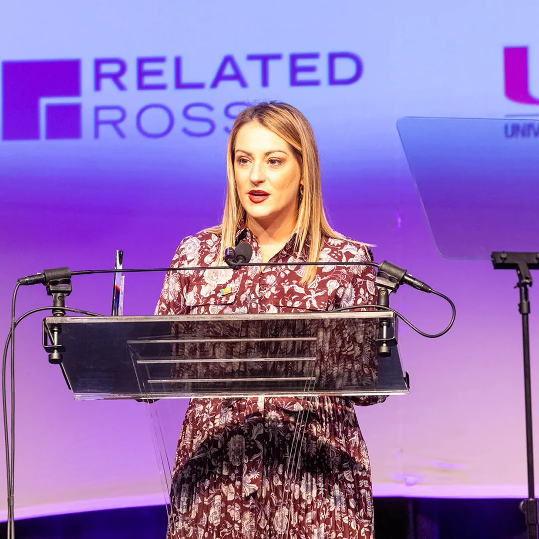 Woman stands at a podium, delivering a speech to an audience.