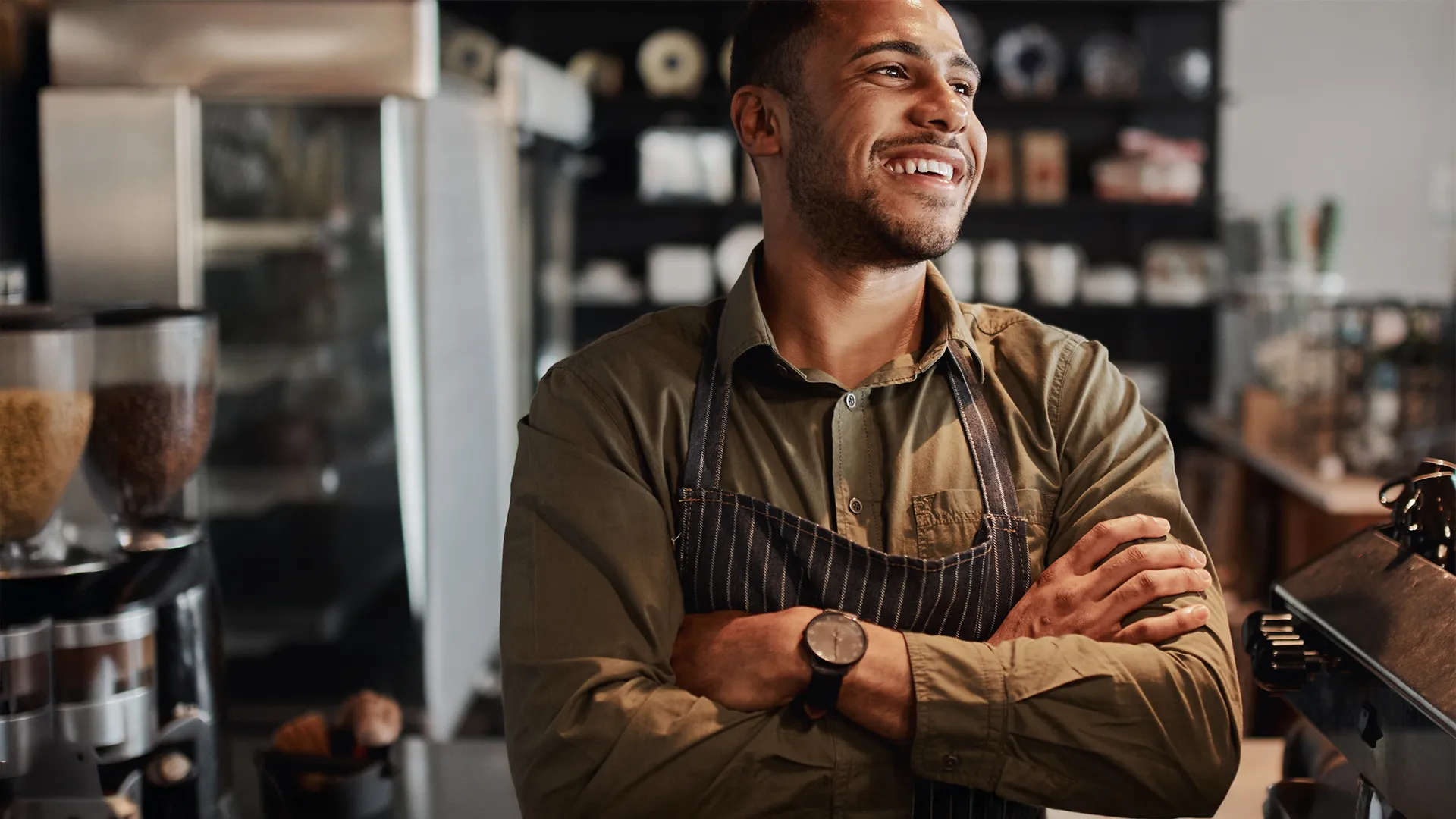 Man smiling wearing an apron stands inside a coffee shop.