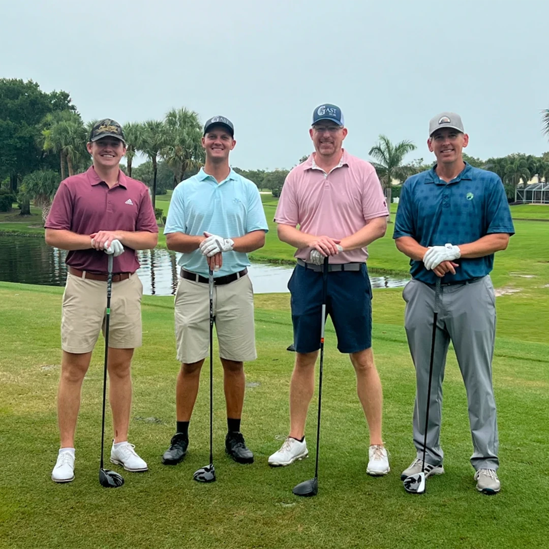 Four men smiling and posing together for a photo on a sunny golf course.